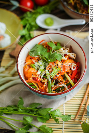 Bowl of stir fried udon noodles garnished with black sesame seeds and fresh mint with green chopsticks 60382451