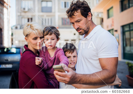 A young family with two small children standing outdoors in town, taking selfie. 60382668