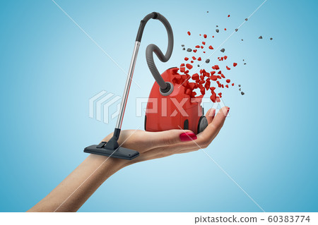 Female hand with red vacuum cleaner shattering into pieces on blue background 60383774