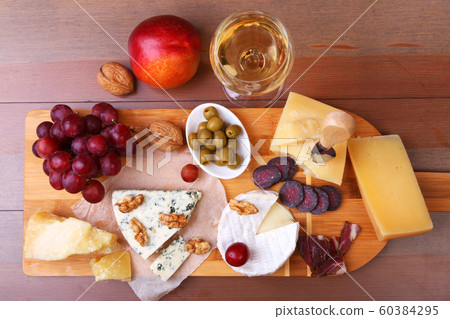Assorted cheeses, nuts, grapes, fruits, smoked meat and a glass of wine on a serving table. Dark and Moody style. Free space for text. Assorted cheeses, nuts, grapes, fruits, smoked meat and a glass of wine on a serving table. Dark and Moody style. Free space for text. 60384295