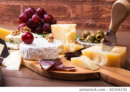 Assortment of cheese with fruits, grapes, nuts and cheese knife on a wooden serving tray. 60384298