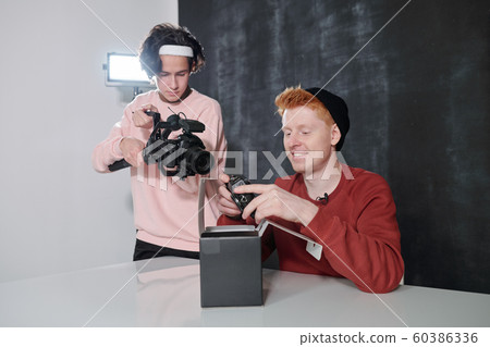 Young cameraman shooting happy male vlogger holding new photocamera Young cameraman shooting happy male vlogger holding new photocamera 60386336