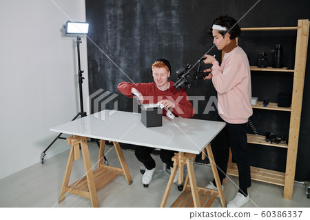 Young cameraman with video equipment shooting male vlogger opening box Young cameraman with video equipment shooting male vlogger opening box 60386337