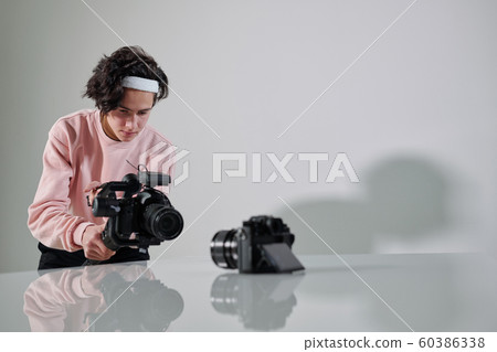 Young serious video blogger standing in front of new photo equipment on desk Young serious video blogger standing in front of new photo equipment on desk 60386338