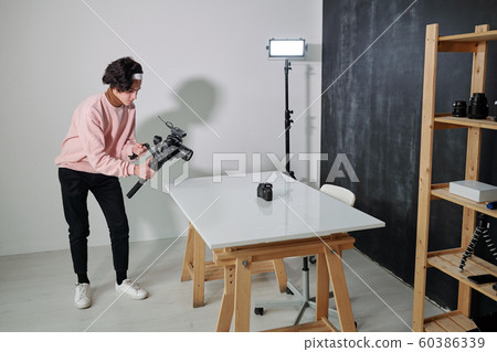 Young casual video blogger shooting new photo equipment in studio Young casual video blogger shooting new photo equipment in studio 60386339