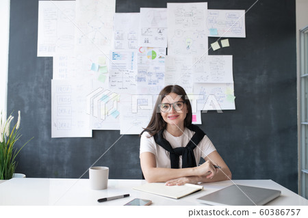 Young successful female economist sitting by desk on background of blackboard 60386757