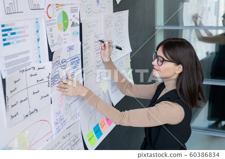 Confident economist analyzing financial information on blackboard in office Confident economist analyzing financial information on blackboard in office 60386834