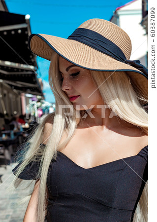 High fashion portrait of a graceful woman in an elegant straw hat and dress that walks along a city street High fashion portrait of a graceful woman in an elegant straw hat and dress that walks along a city street 60387099