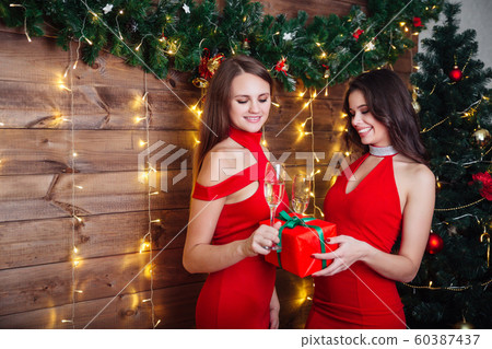 portrait of two happy joyful girls in red dresses toasting with champagne glasses over Christmas background 60387437