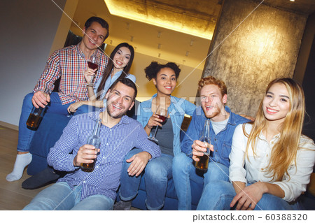 Group of friends having party indoors fun together sitting on coach drinking Group of friends having party indoors fun together sitting on coach drinking 60388320