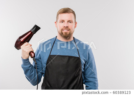 Young bearded hairdresser in apron and blue pullover holding hairdryer 60389123