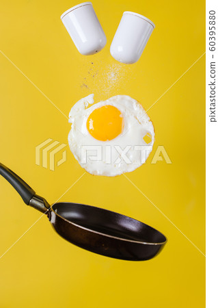 Breakfast time. A fried egg and a frying pan with salt shakers levitate in the air on a yellow Breakfast time. A fried egg and a frying pan with salt shakers levitate in the air on a yellow 60395880