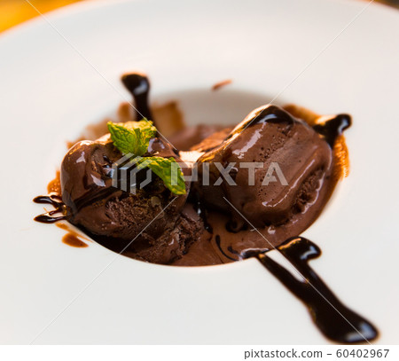Tasty cold chocolate ice cream served at plate with chocolate cream and mint Tasty cold chocolate ice cream served at plate with chocolate cream and mint 60402967