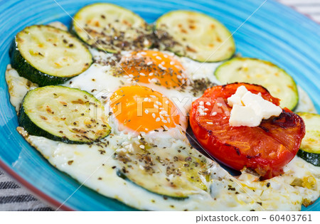 Close up of cooked eggs with tomatoes and zucchini at blue plate 60403761