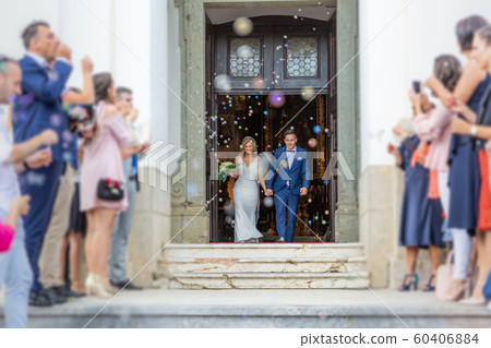Newlyweds exiting the church after the wedding ceremony, family and friends celebrating their love with the shower of soap bubbles, custom undermining traditional rice bath Newlyweds exiting the church after the wedding ceremony, family and friends celebrating their love with the shower of soap bubbles, custom undermining traditional rice bath 60406884