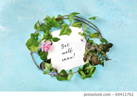 Get well soon card with a wreath of green ivy leaves and a tender pink rose, overhead shot on a blue background 60411762
