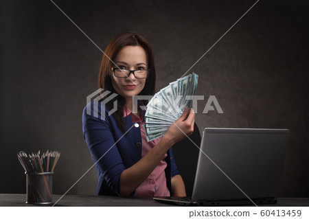 Successful businesswoman at the table on a dark background with laptop and money. Successful businesswoman at the table on a dark background with laptop and money. 60413459