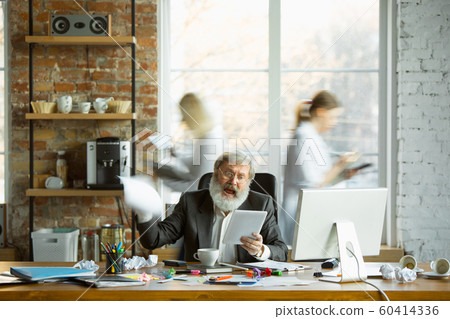 Nervous and tired boss at his workplace busy while people moving near blurred 60414336