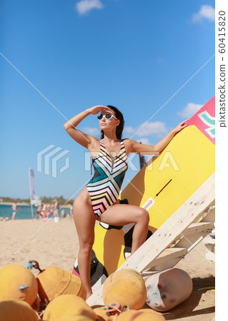 A surf athlete in a sports swimsuit and sunglasses on a sandy beach 60415820