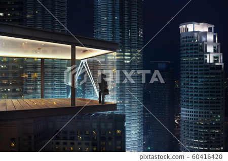 Businessman in an modern sky office by night with beautiful city skyline view . 60416420