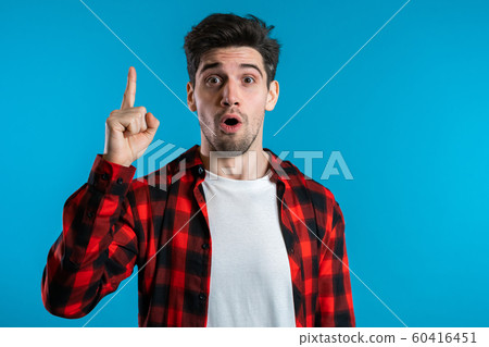 Portrait of young thinking pondering man in red having idea moment pointing finger up on blue studio background. Smiling happy student guy showing eureka gesture. Portrait of young thinking pondering man in red having idea moment pointing finger up on blue studio background. Smiling happy student guy showing eureka gesture. 60416451
