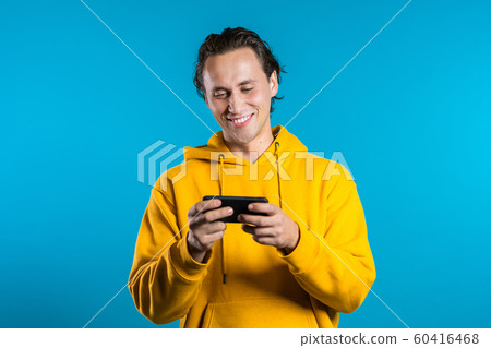 Man sms texting using app on smartphone. Handsome young guy surfing internet with mobile phone. Blue studio background Man sms texting using app on smartphone. Handsome young guy surfing internet with mobile phone. Blue studio background 60416468