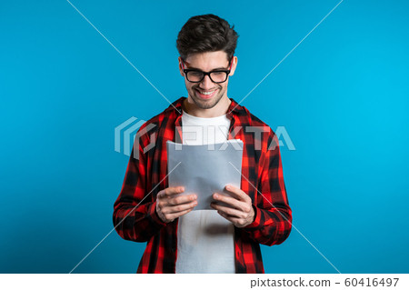 Young handsome man checks documents, utility bills, report. Businessman isolated on blue background. He is satisfied with work of corporate staff. Young handsome man checks documents, utility bills, report. Businessman isolated on blue background. He is satisfied with work of corporate staff. 60416497
