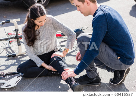 Helpful young man giving first aid to an injured woman after bicycle accident Helpful young man giving first aid to an injured woman after bicycle accident 60416587