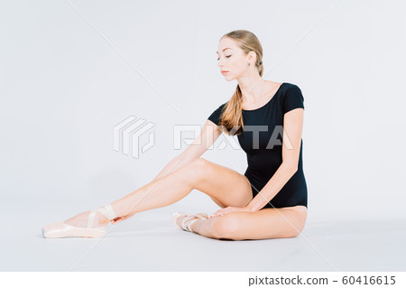 Ballerina wraps white silk ribbons of soft top ballet shoes pointe and ties them up. Woman preparing for dance training lessons in gym. 60416615