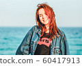 Nice girl with red hair smiling. Modern youth. Casual style, denim clothing. Away blue sea. Copy space. Solar lighting. 60417913