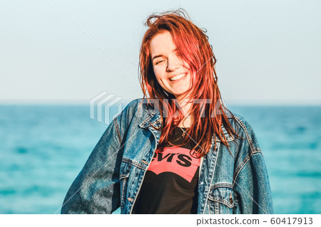 Nice girl with red hair smiling. Modern youth. Casual style, denim clothing. Away blue sea. Copy space. Solar lighting. 60417913