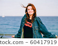 Nice girl with red hair smiling. Modern youth. Casual style, denim clothing. Away blue sea. Copy space. Solar lighting. 60417919