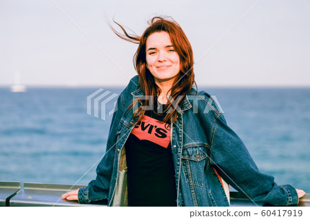 Nice girl with red hair smiling. Modern youth. Casual style, denim clothing. Away blue sea. Copy space. Solar lighting. 60417919