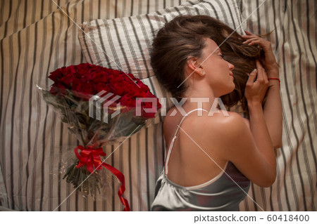 Good morning Attractive young woman with bouquet of hundreds of red roses is sleeping at home. 60418400