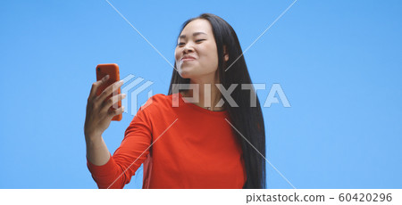 Young woman using smartphone as a mirror 60420296