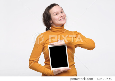 Young caucasian woman in yellow clothes showing screen of tablet with copyspace for your text. 60420630
