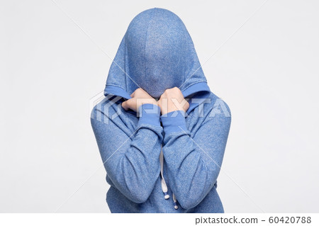 Teenager hiding her face under blue sweater being frightened and stressed Teenager hiding her face under blue sweater being frightened and stressed 60420788