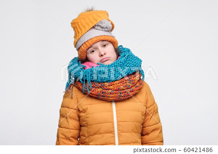 Young woman in several hats and scarfs does not like winter time looking at camera with sad expression. Young woman in several hats and scarfs does not like winter time looking at camera with sad expression. 60421486