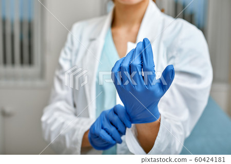 Close up of a female doctor putting a blue latex gloves on a clinic background. Close up of a female doctor putting a blue latex gloves on a clinic background. 60424181