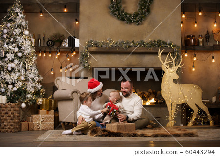 Photo of happy parents with sons at fireplace, deer with garland in room 60443294