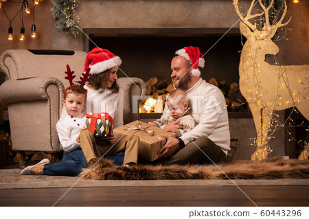 Photo of happy parents with sons at fireplace, deer with garland in room 60443296