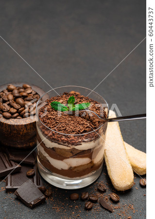 Classic tiramisu dessert in a glass cup and pieces of chocolate on dark concrete background Classic tiramisu dessert in a glass cup and pieces of chocolate on dark concrete background 60443737