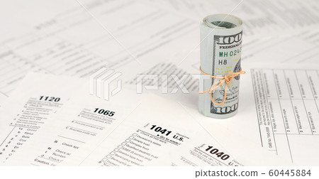 Tax forms lies near roll of hundred dollar bills. Tax forms lies near roll of hundred dollar bills. 60445884