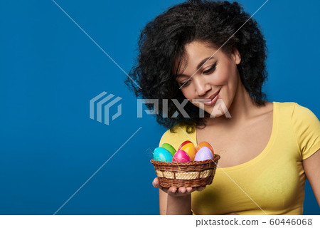 Smiling woman holding a basket with colorful Easter eggs Smiling woman holding a basket with colorful Easter eggs 60446068