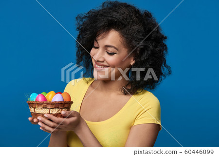 Smiling woman holding a basket with colorful Easter eggs Smiling woman holding a basket with colorful Easter eggs 60446099