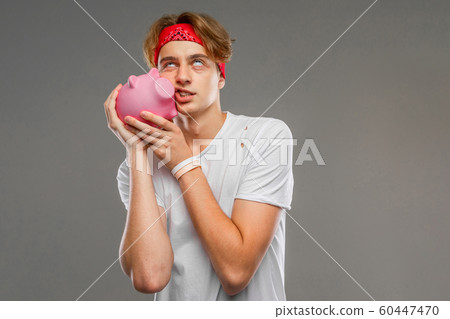 Young caucasian man in red sunglasses, white t-shirt with pink pig money box isolated on grey Young caucasian man in red sunglasses, white t-shirt with pink pig money box isolated on grey 60447470