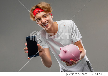 Young caucasian man in red sunglasses, white t-shirt with pink pig money box isolated on grey 60447485