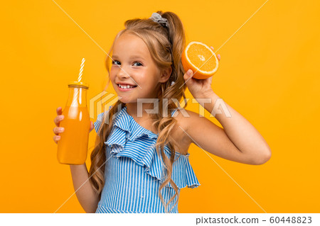 funny girl holding a sliced orange and a bottle of juice in her hands on a yellow background 60448823