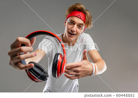 Young caucasian man in red sunglasses, white t-shirt listen to music with big red earphones isolated 60448881