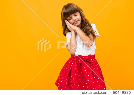 Caucasian girl in a skirt shows that she wants to sleep on a yellow background Caucasian girl in a skirt shows that she wants to sleep on a yellow background 60449820